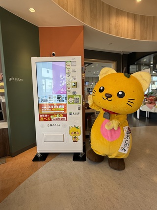 ふるさと納税の自販機を誇らしげに指さすゆずにゃん